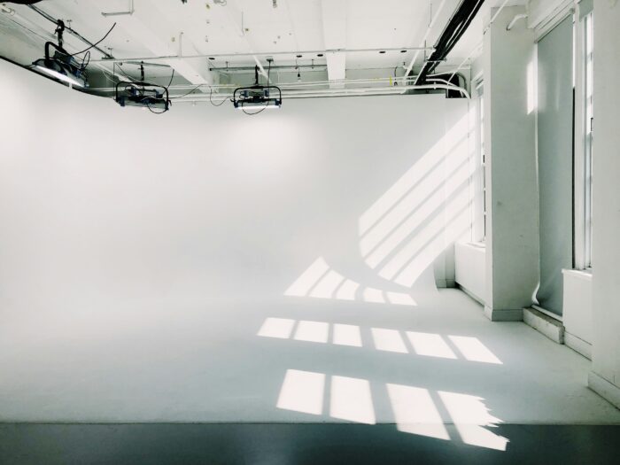 Empty white cyclorama studio with overhead lighting rigs and natural light casting window shadows across the floor