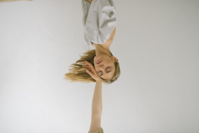 In a white room, two women are positioned upside down, adding an element of whimsy to the scene.
